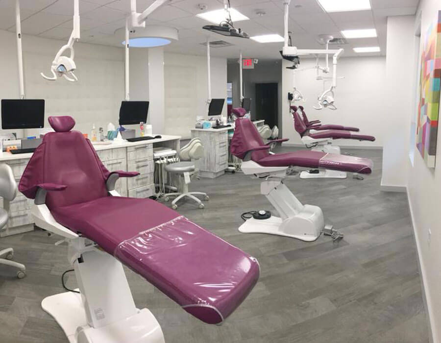 large dental examination room with white and purple chairs and a grey floor