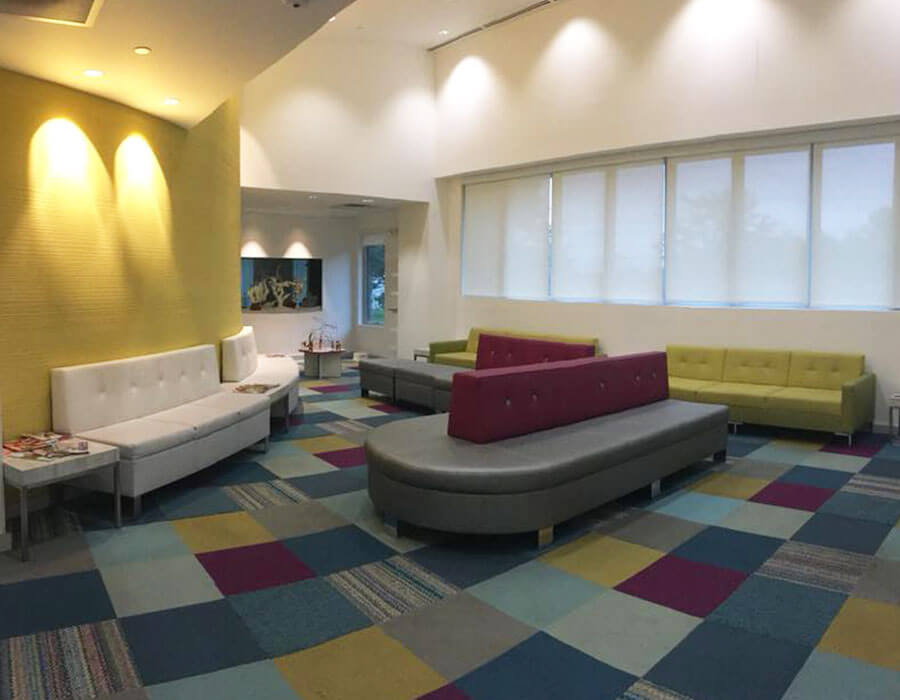 waiting room with grey, green and tan seating, multi-colored carpeting and yellow walls