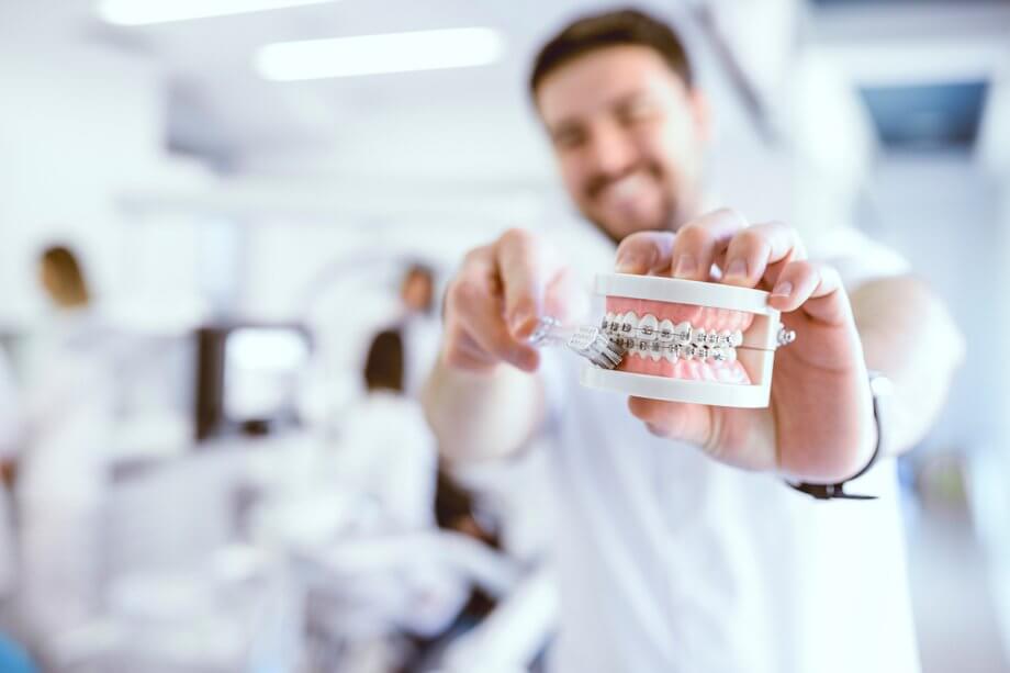 a man demonstrates brushing teeth with braces on model teeth