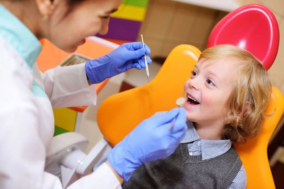 young boy in orange dental exam chair smiling up at the dentist