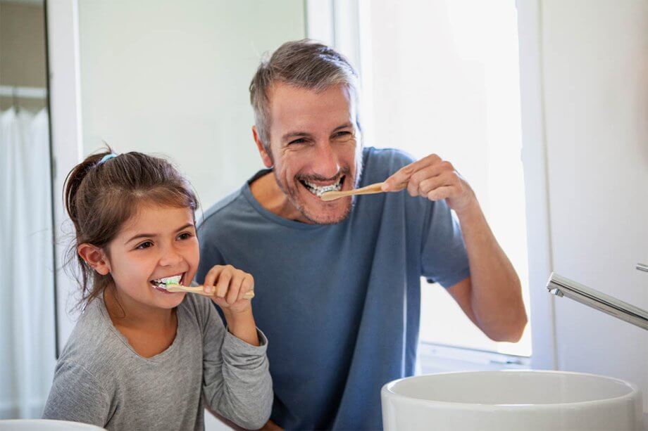 child with parent brushing teeth