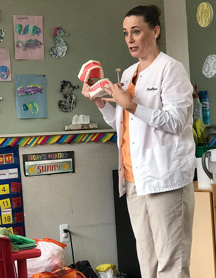 staff member in an elementary classroom holding a large model of teeth