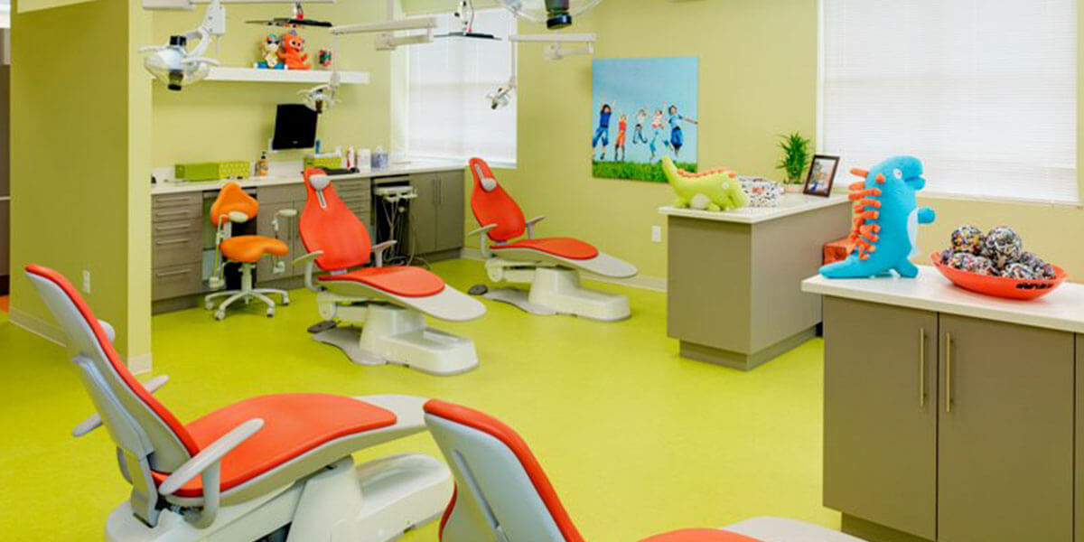 green dental examination room with orange and white chairs with toy dinosaurs on counter