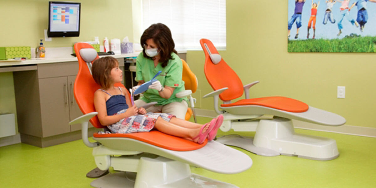 child in dental exam chair with hygienist showing her a blue mirror