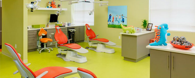 green dental examination room with orange and white chairs with toy dinosaurs on counter