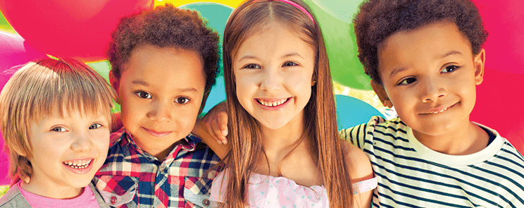 close up of two boys and two girls standing in front of colorful balloons, smiling