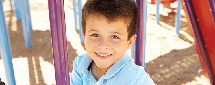 young boy in blue polo shirt smiling on a playground