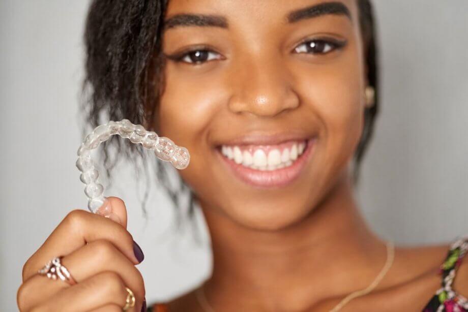close up of teen girl smiling, holding invisalign piece in her hand
