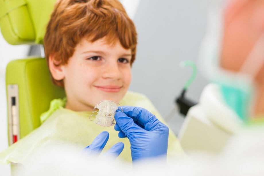 a dentist holds a retainer in front of a boy