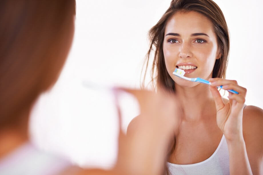 a woman brushes her teeth in the mirror